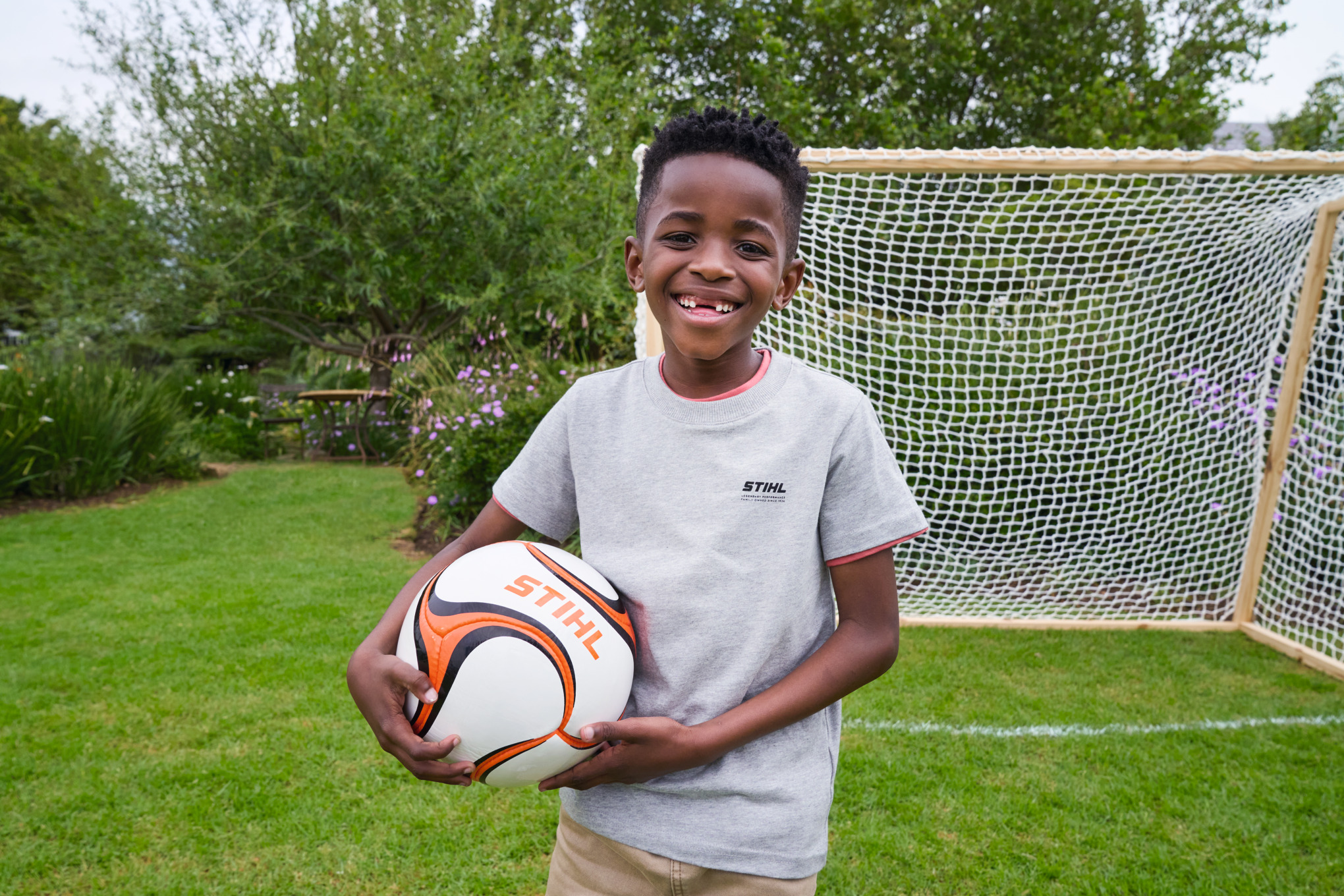 Un garçon rayonnant tient un ballon de football STIHL dans la main devant le nouveau but